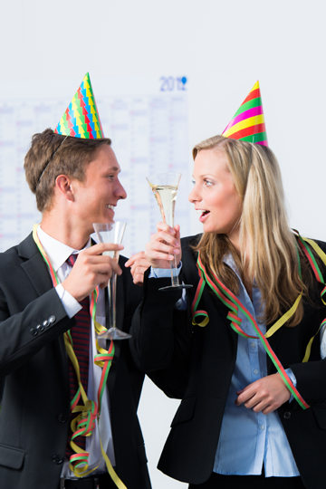 Zwei Personen mit Partyhüten und Sektgläsern in der Hand schauen sich fröhlich an.