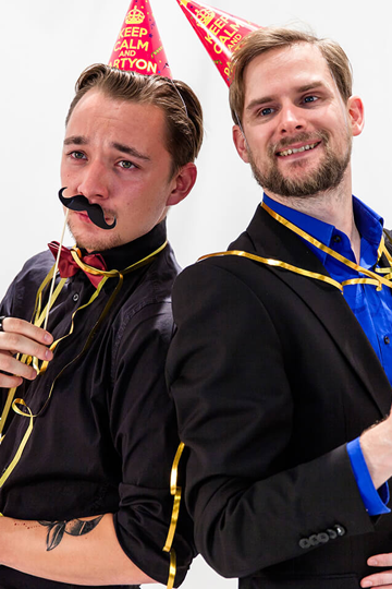 Zwei Männer posieren Rücken an Rücken mit Partyhüten und Props vor der Fotobox.