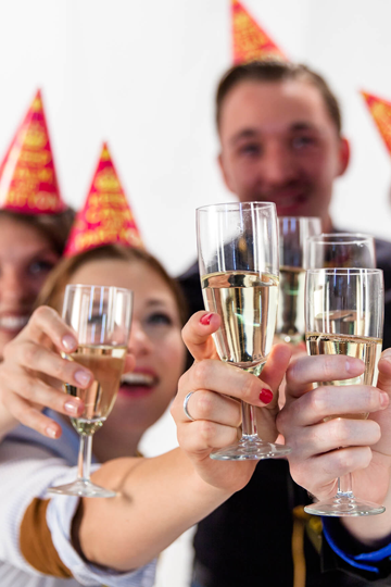 Personen mit Partyhüten halten Sektgläser in die Kamera zum anstoßen.