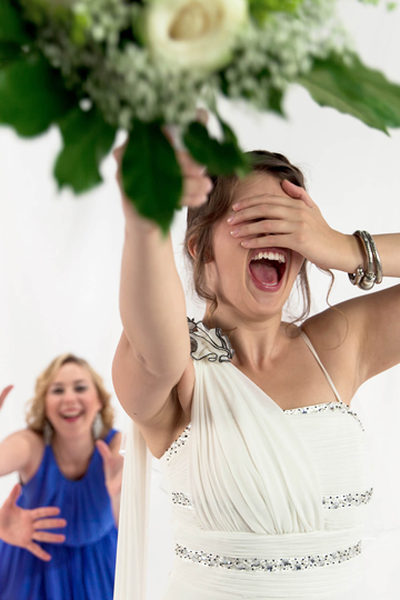 Eine Braut hält sich die Augen zu und wirft den Brautstrauß nach hinten.
