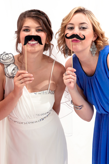 Zwei Frauen posieren mit Schnurrbart-Props vor der Kamera.