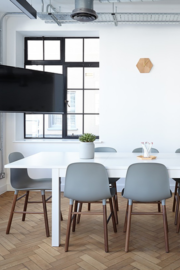 Helles freundliches Büro mit weißen Stühlen, einem Tisch und Monitor an der Wand.