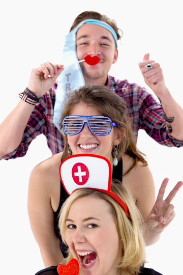 Drei glückliche Personen mit Requisiten stehen hintereinander und schauen über die Köpfe der vorderen Person.